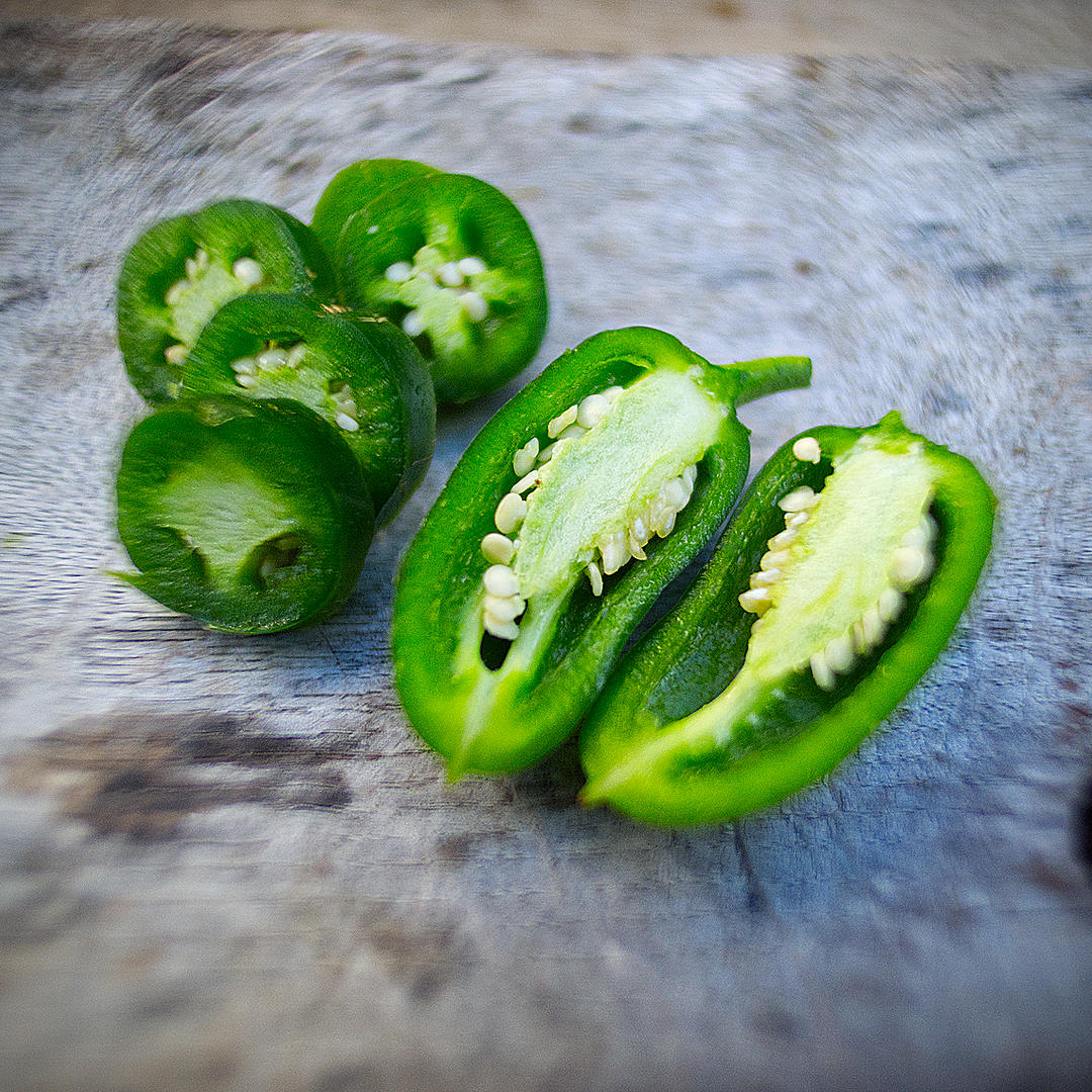  World of Chillies: Fresh green jalapeño chillies sliced open to reveal their thick flesh and seeds. 