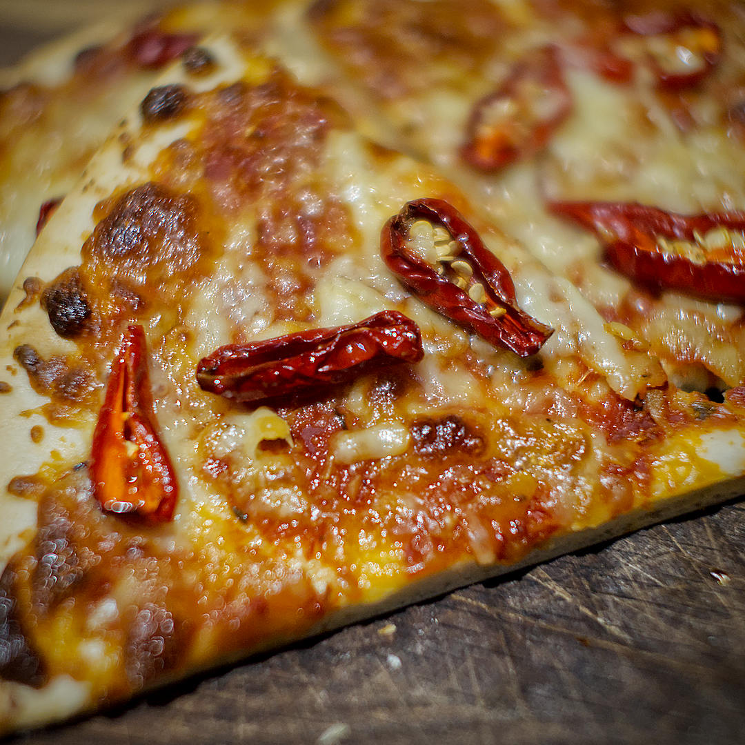  1. World of Chillies: Close-up of roasted red Raging Bull chilli slices on a golden, bubbling cheese pizza. 