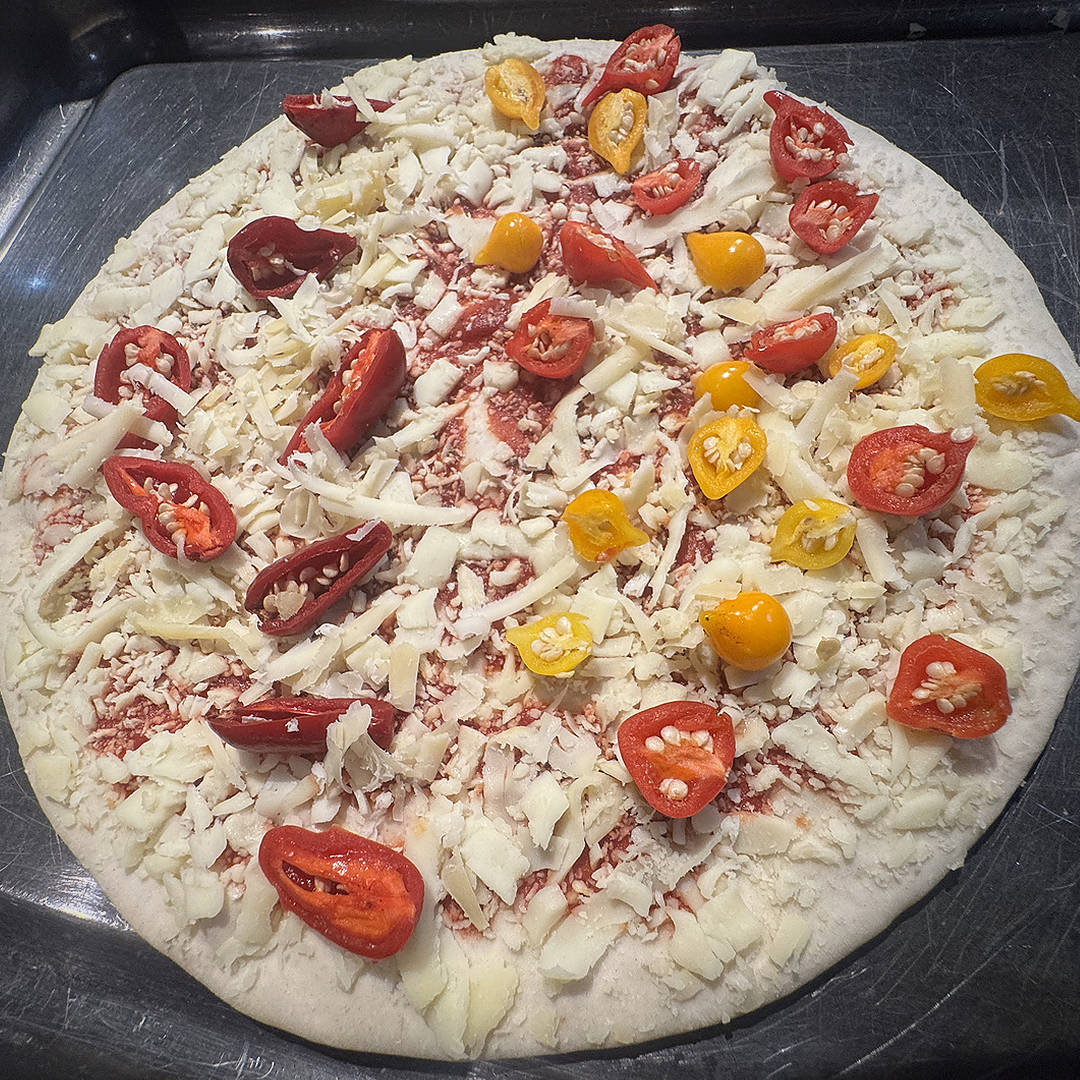  World of Chillies: Uncooked homemade pizza generously topped with sliced Raging Bull chillies and grated cheese. 